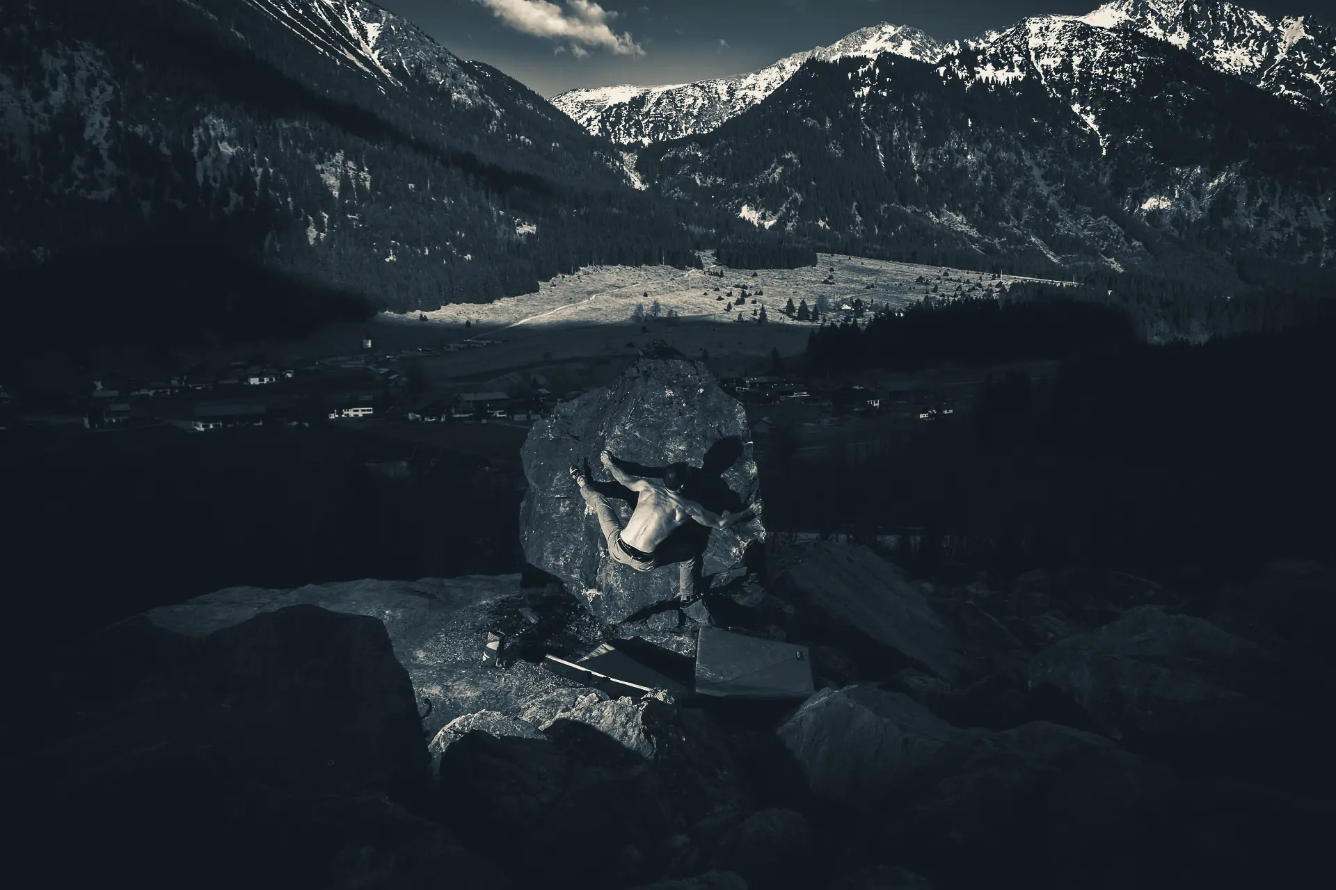 Boulderer an einem Felsblock vor Alpenpanorama, Crashpads am Boden